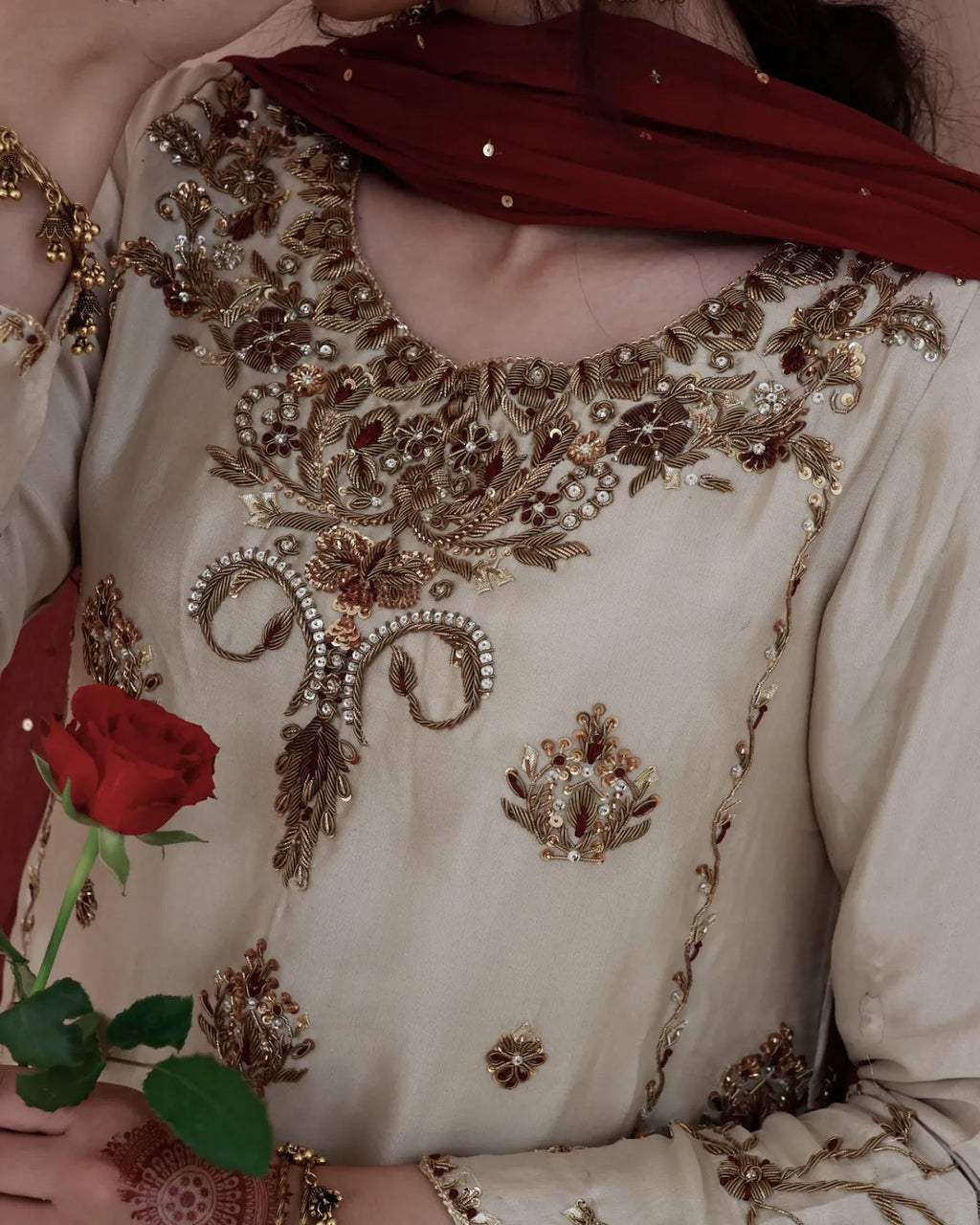 Close-up of a person wearing a heavily embroidered traditional outfit with a red rose held in hand.