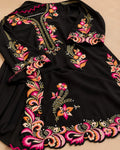 A black long-sleeve tunic or kurta with vibrant floral and paisley embroidery in pink, orange, yellow, and green, laid flat on a beige background.