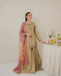 Woman in traditional beige and pink outfit standing next to a table with fruits and candles.