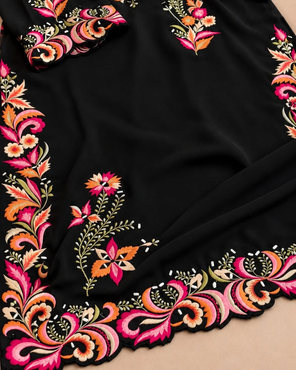 A close-up of a black fabric garment or textile featuring ornate multicolor floral and paisley embroidery along the border, with a matching embroidered cuff or sleeve detail visible at the top left.