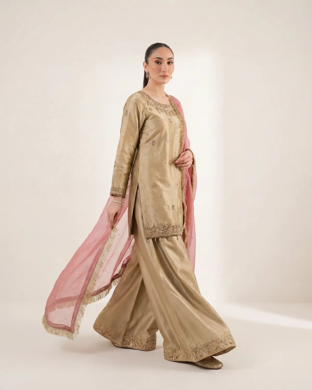 Woman wearing a traditional beige outfit with pink dupatta on a white background