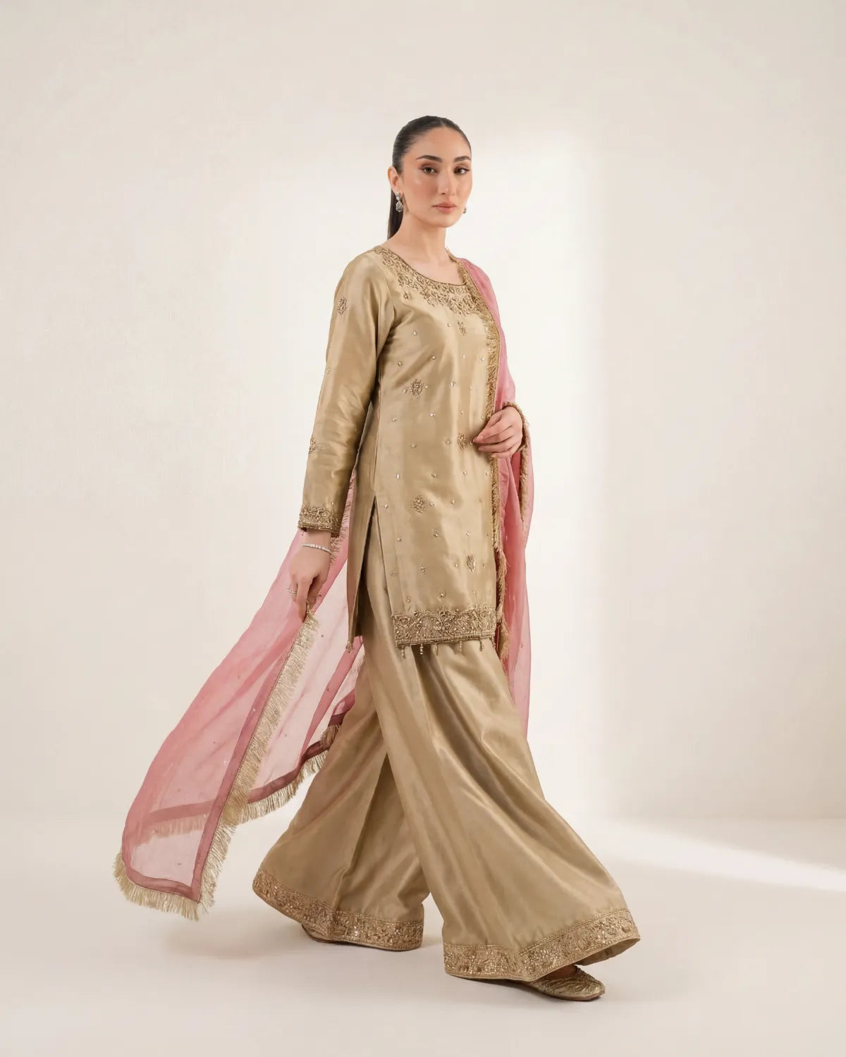Woman wearing a traditional beige outfit with pink dupatta on a white background