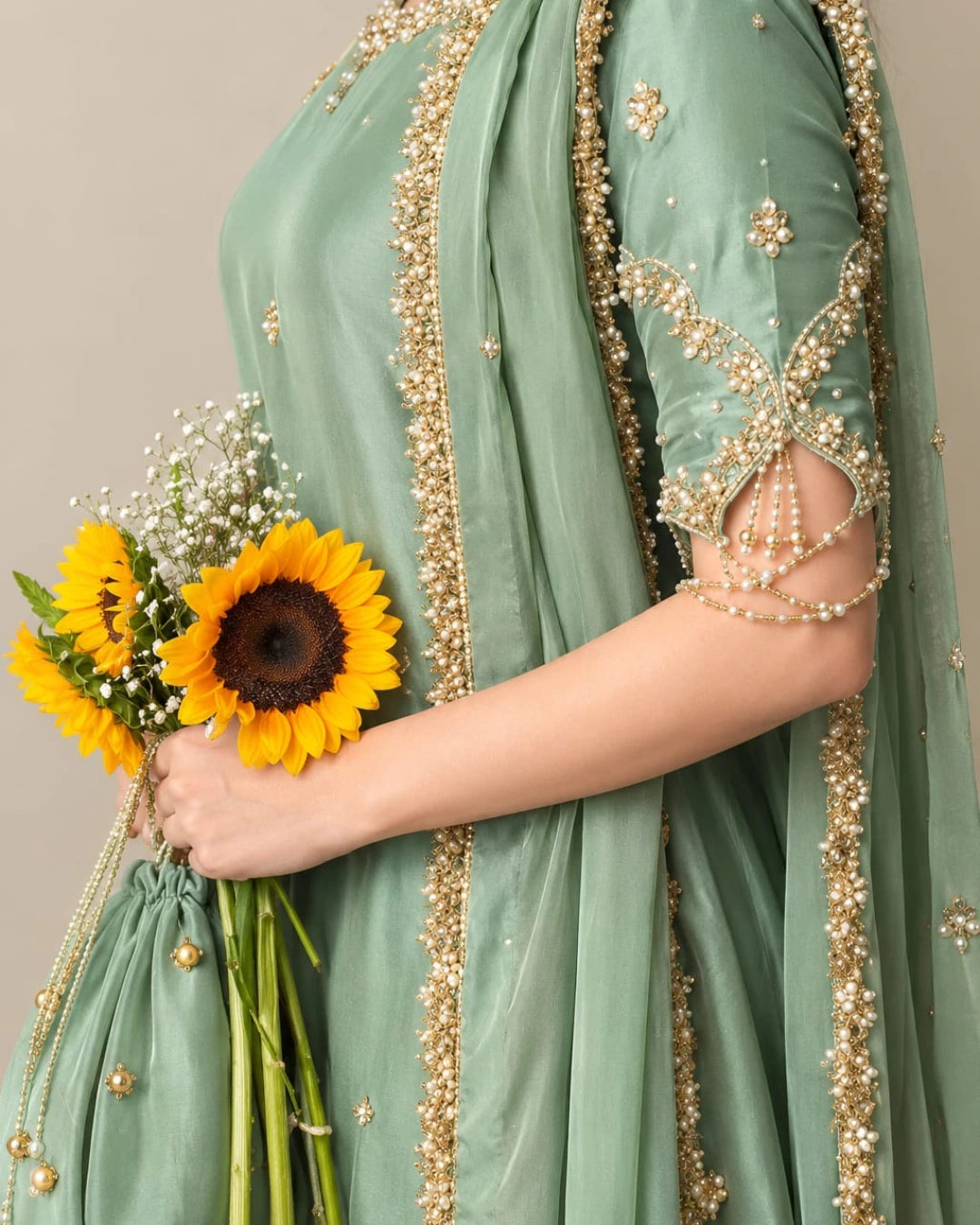 QAM Style luxury ethnic wear showcasing a sage green silk outfit with intricate golden embroidery, ornate borders, and a graceful traditional silhouette.