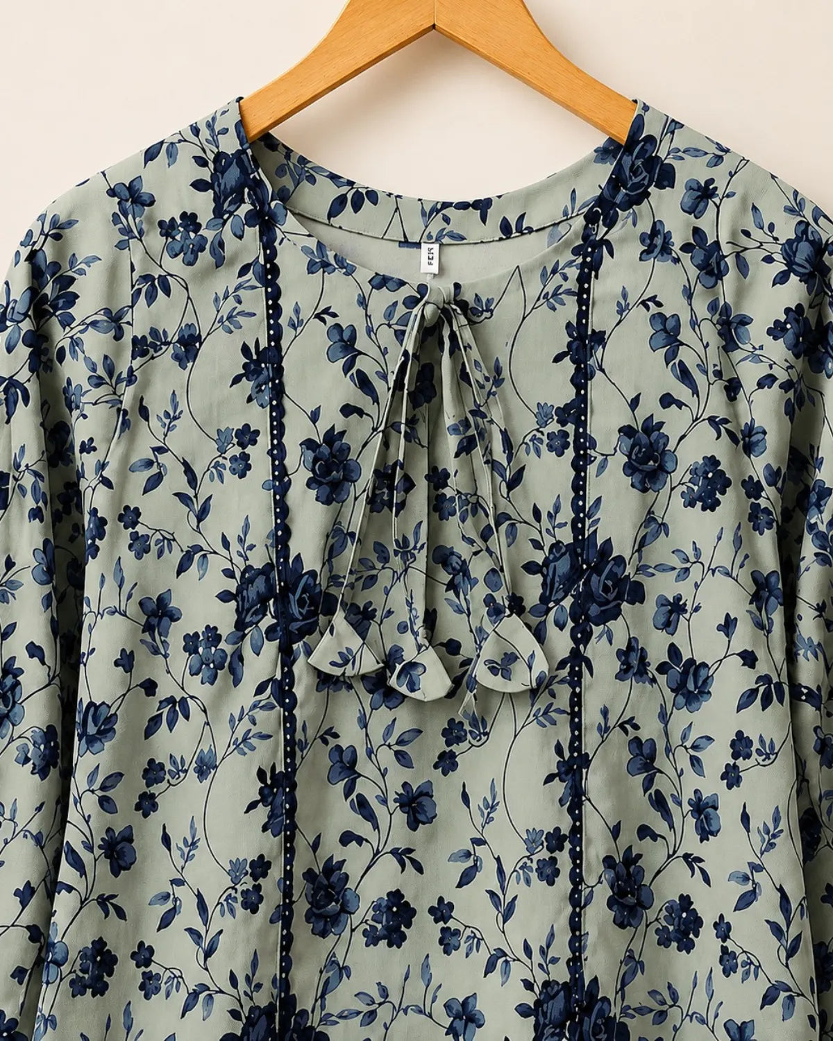 Floral patterned blouse on a wooden hanger against a white background