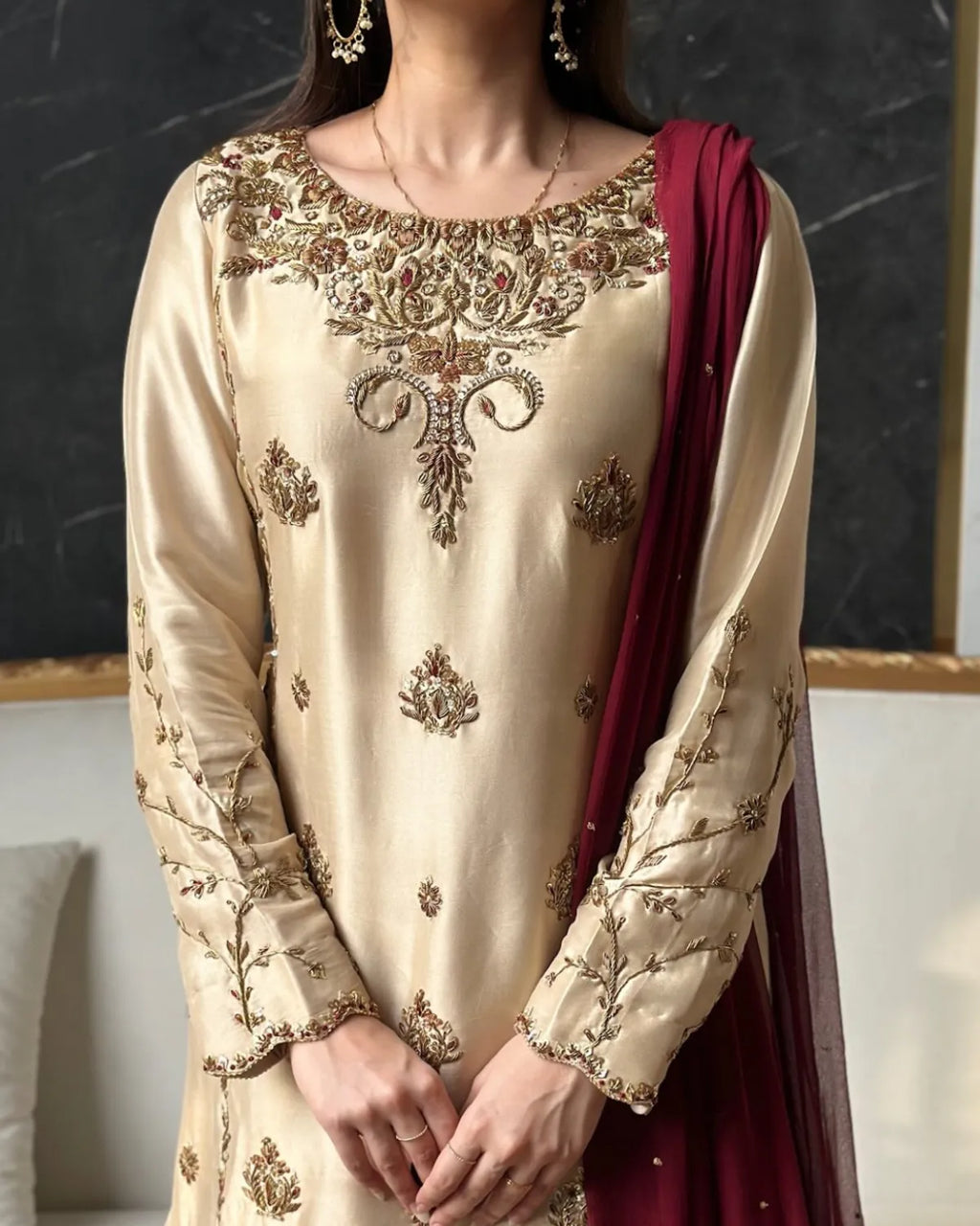 Beige embroidered traditional outfit with maroon dupatta against a dark background