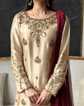 Beige embroidered traditional outfit with maroon dupatta against a dark background