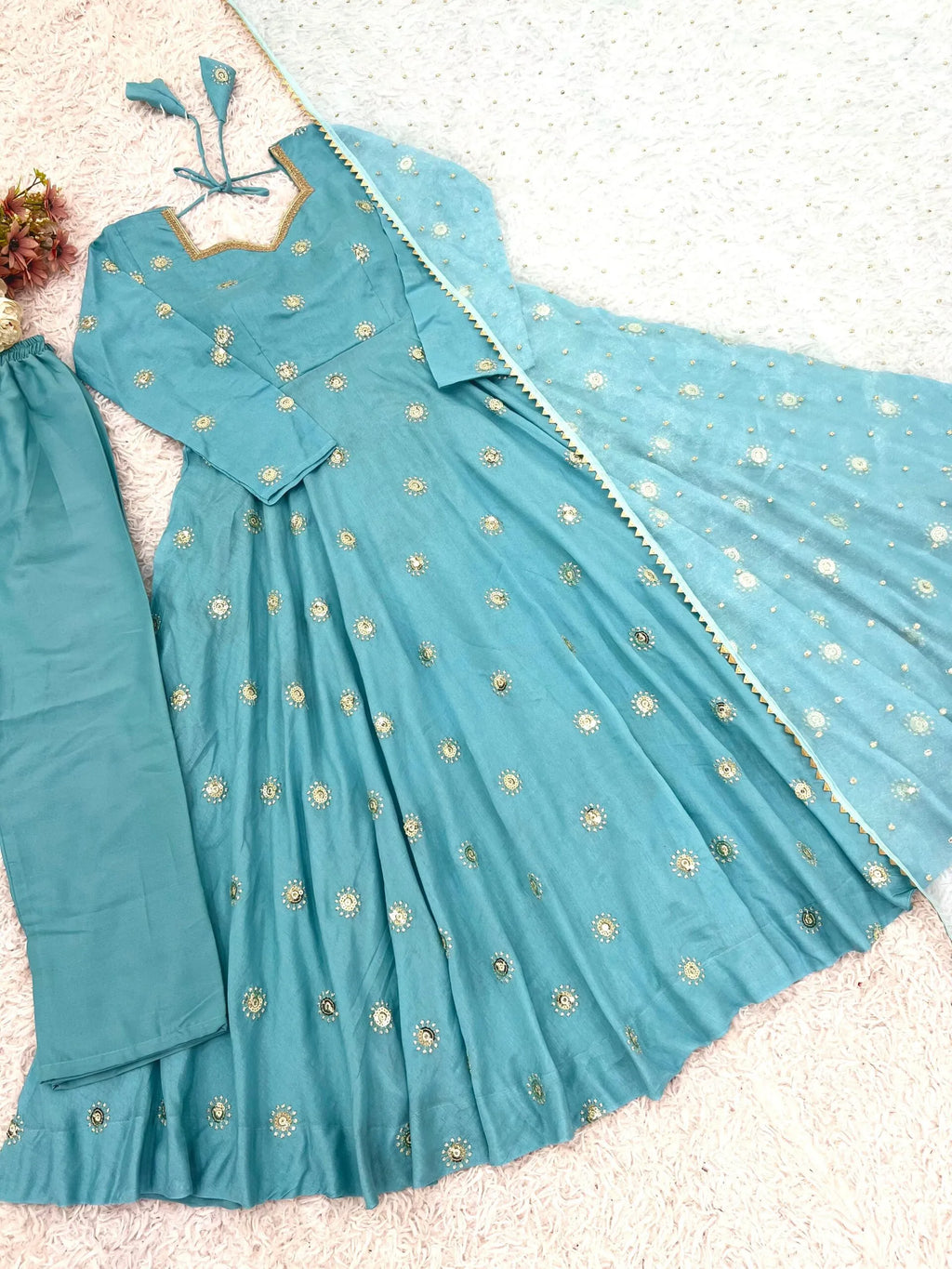 A light blue anarkali gown with gold floral embroidery, matching pants, and a dupatta, laid out on a textured white surface.