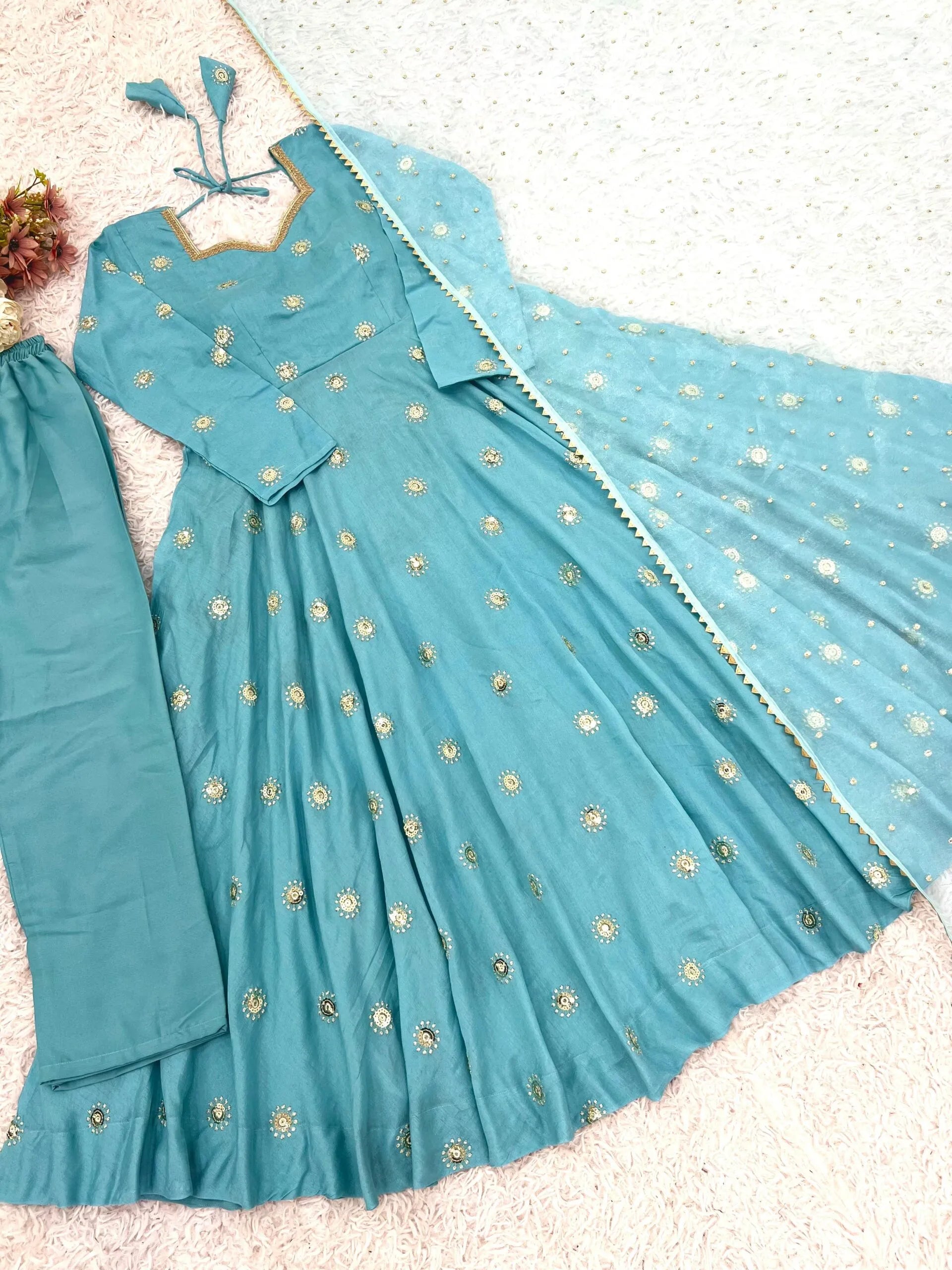 A light blue anarkali gown with gold floral embroidery, matching pants, and a dupatta, laid out on a textured white surface.