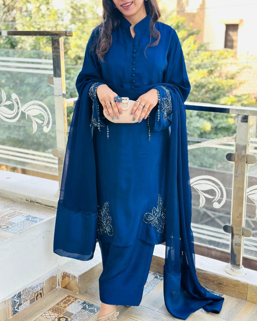 A woman wearing a royal blue traditional Indian outfit with a matching dupatta, standing on an outdoor balcony with a glass railing.