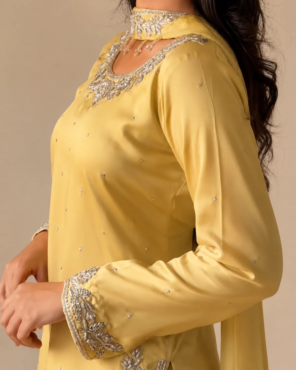 A close-up of a woman wearing a yellow traditional kurta with silver embroidery on the neckline, cuffs, and scattered as small embellishments on the fabric.
