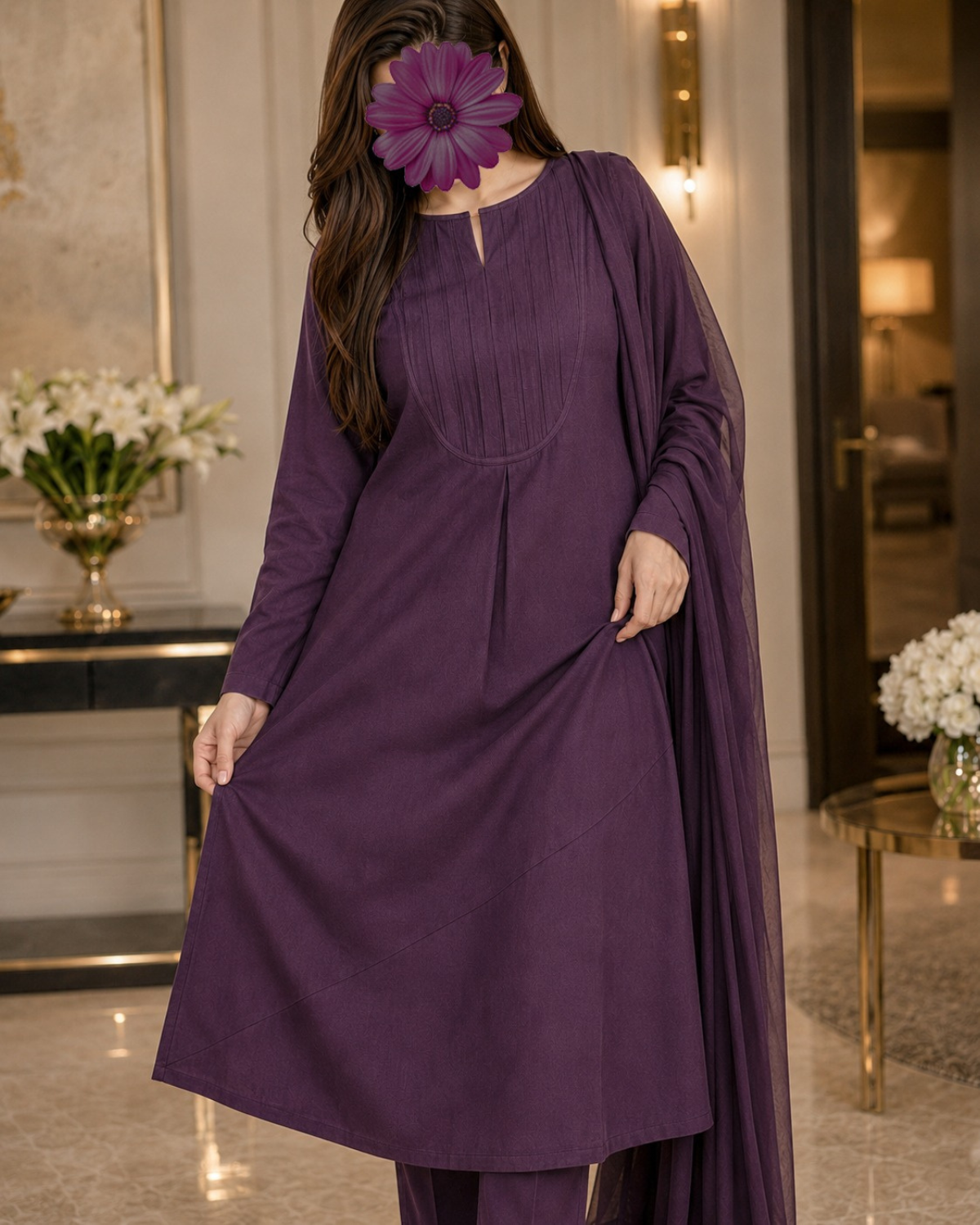 A woman wearing a long-sleeve purple kurta with matching pants and a sheer draped overlay, standing in an indoor room with decorative flowers and warm lighting.