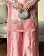 A close-up of a person wearing a pink traditional outfit with silver embroidery and holding a silver beaded clutch purse in an indoor setting.