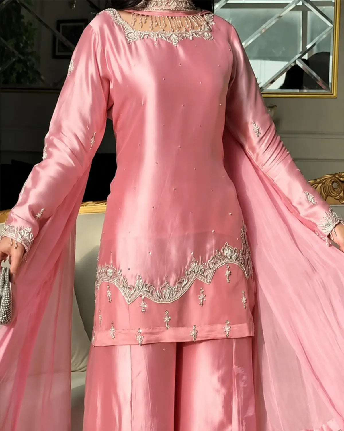 A pink traditional outfit with a matching dupatta, featuring silver embroidered details on the neckline, cuffs, and hem, worn by a model in an indoor setting.