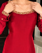 A close-up of a woman wearing a bright red satin dress with gold and red embroidered detailing around the square neckline and on the cuffs.