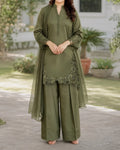 Woman wearing an olive green traditional outfit with floral embroidery in a garden setting.