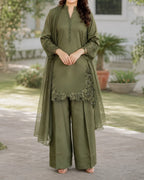 Woman wearing an olive green traditional outfit with floral embroidery in a garden setting.