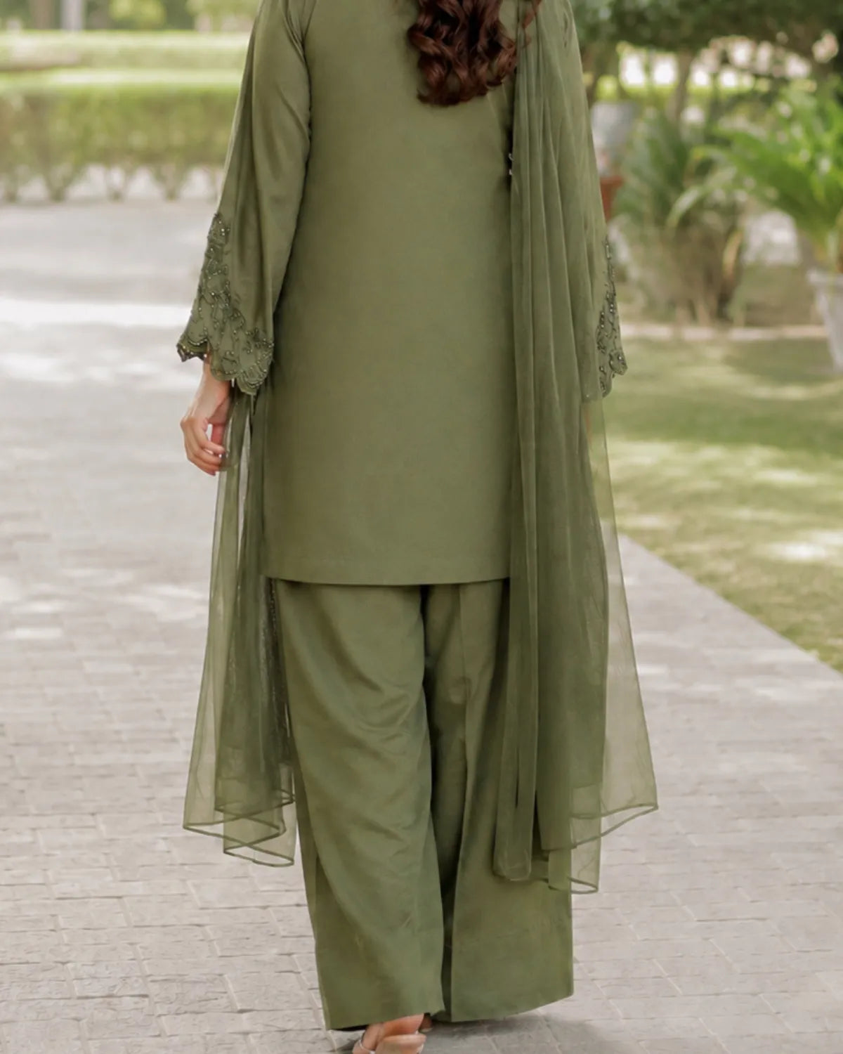 Person wearing an olive green traditional outfit with a long sheer dupatta in an outdoor setting.
